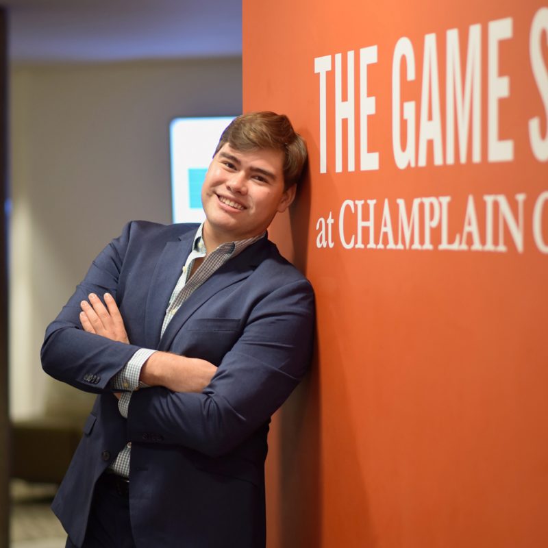 Smiling student in a suit leaning on an orange wall